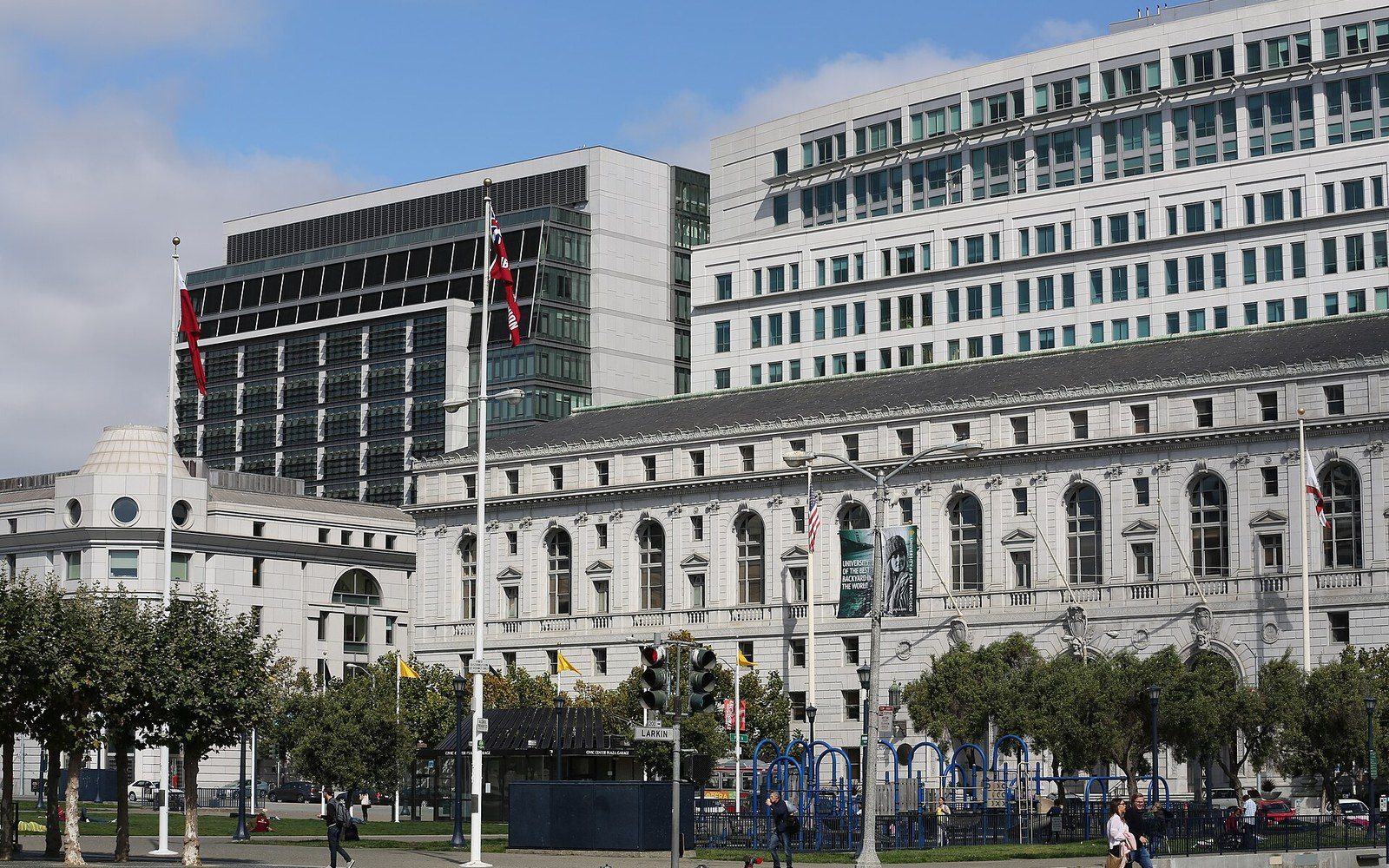 Classical courthouse building fronted by trees and flags, with modern office towers rising behind it