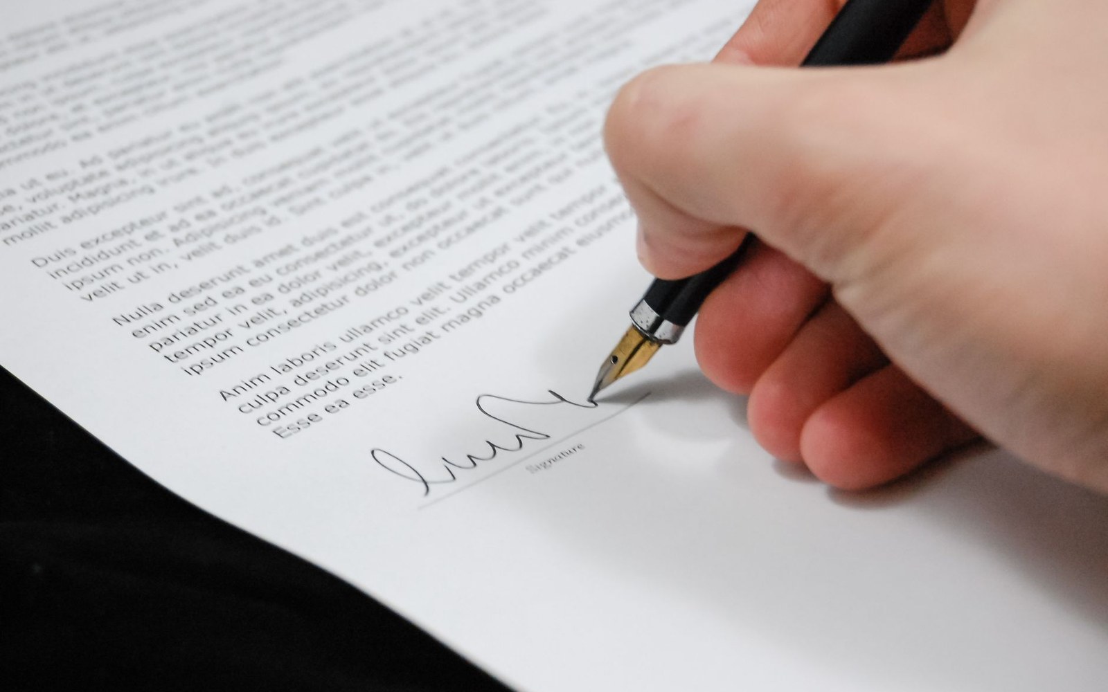 A hand using a fountain pen to sign a printed document