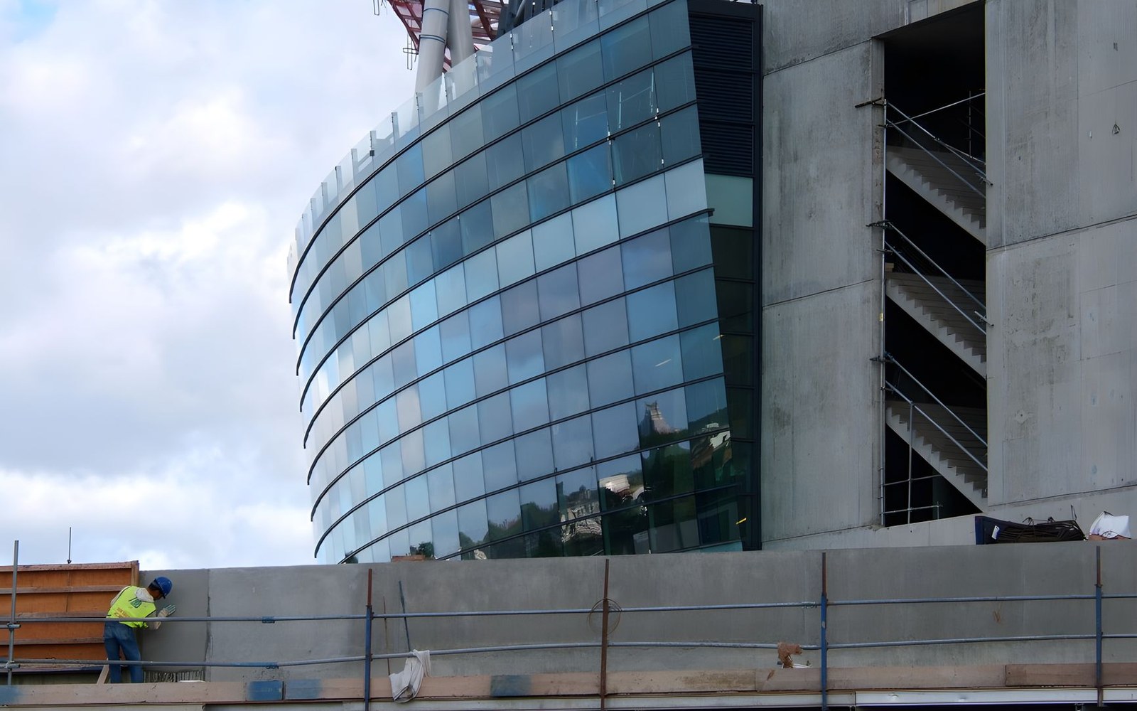 Construction worker on scaffolding beside a curved glass office tower under construction