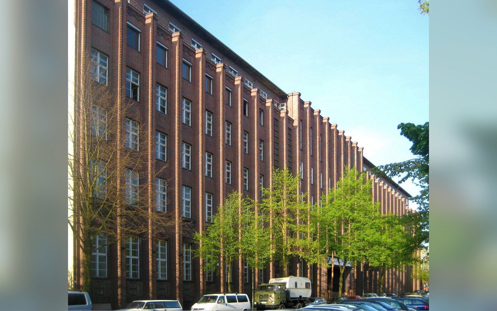 Long brick industrial building with repeating vertical piers and rows of tall windows