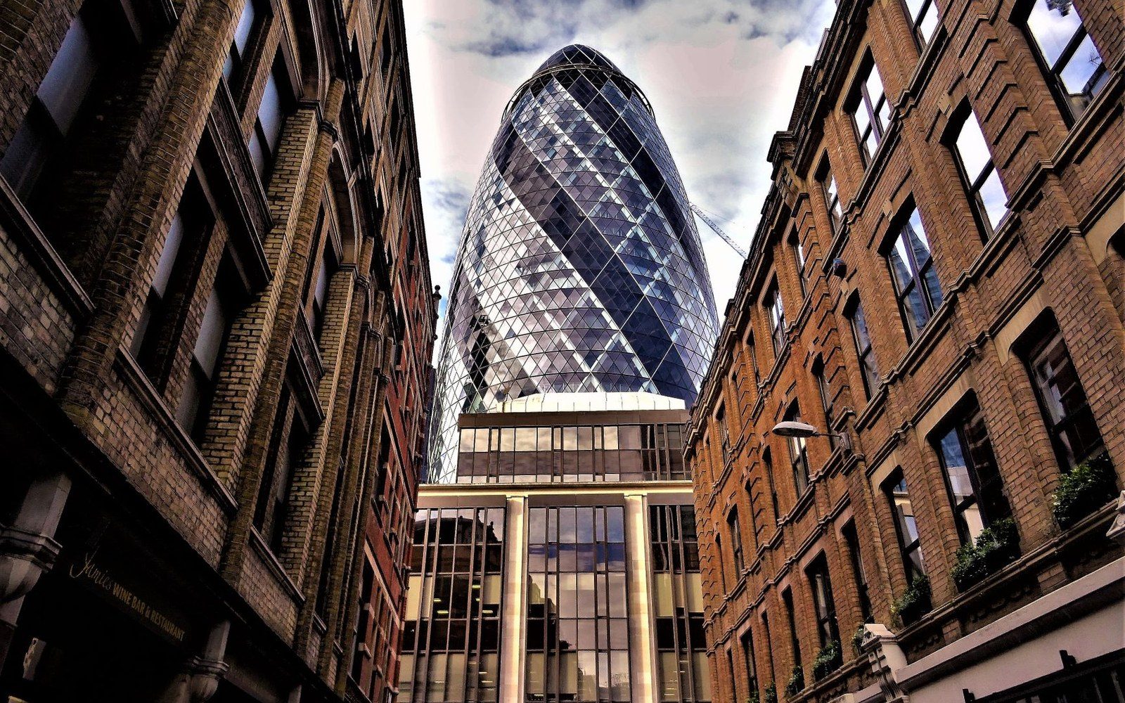 The Gherkin skyscraper rises between narrow brick buildings on a London street