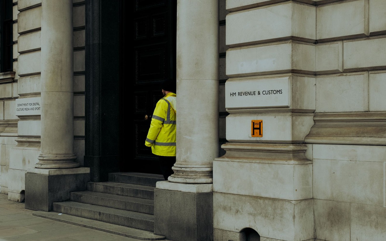 A person in a hi-vis jacket enters the HM Revenue & Customs building through its columned entrance