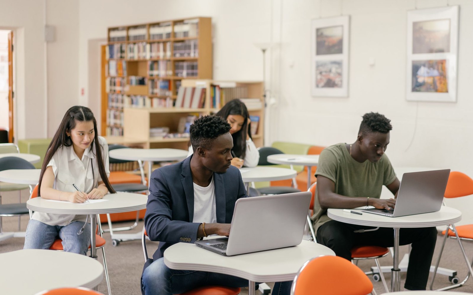 Students work on laptops and take notes at round tables in a library