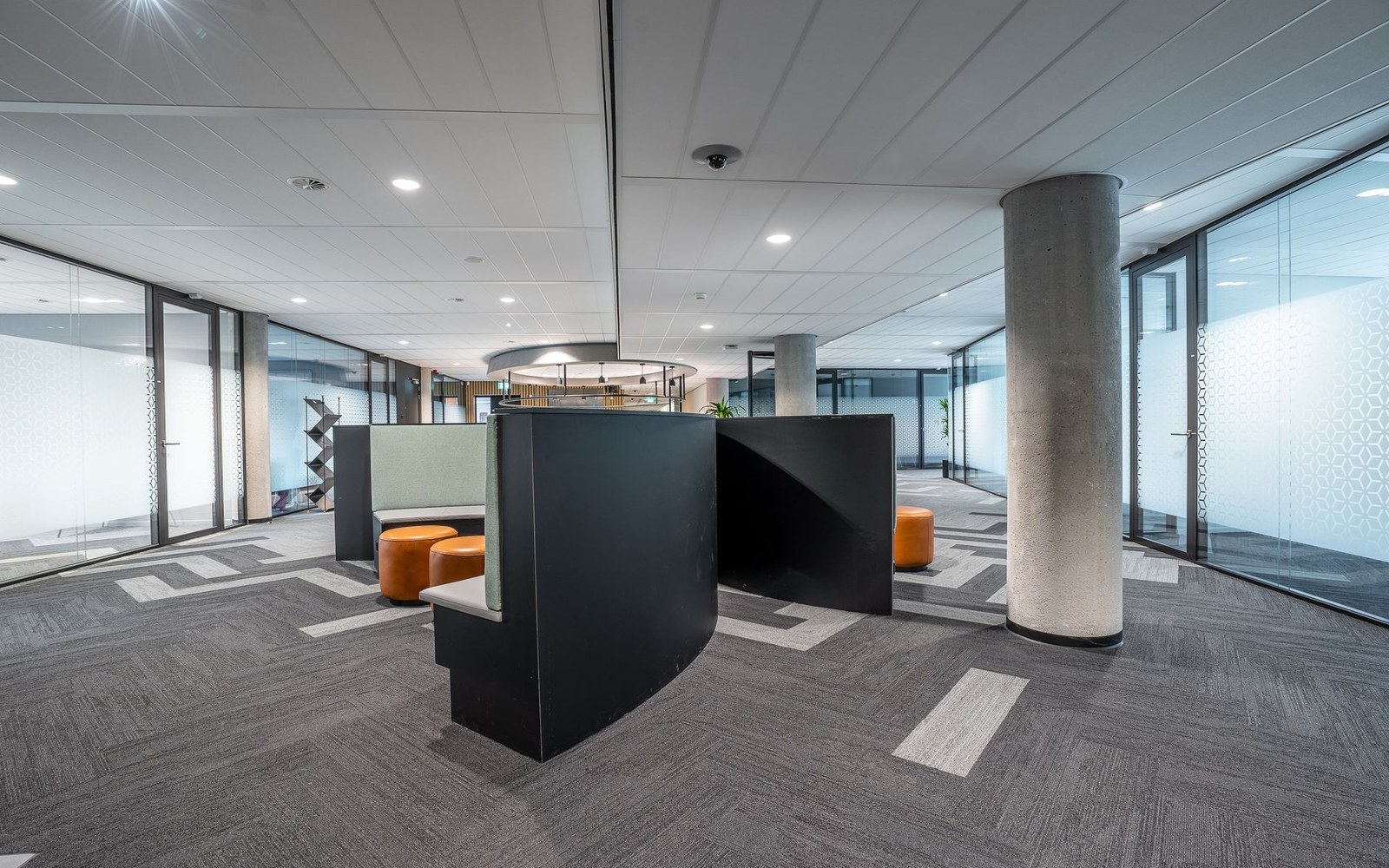 Open-plan office with curved black booth seating, orange stools and patterned carpet tiles