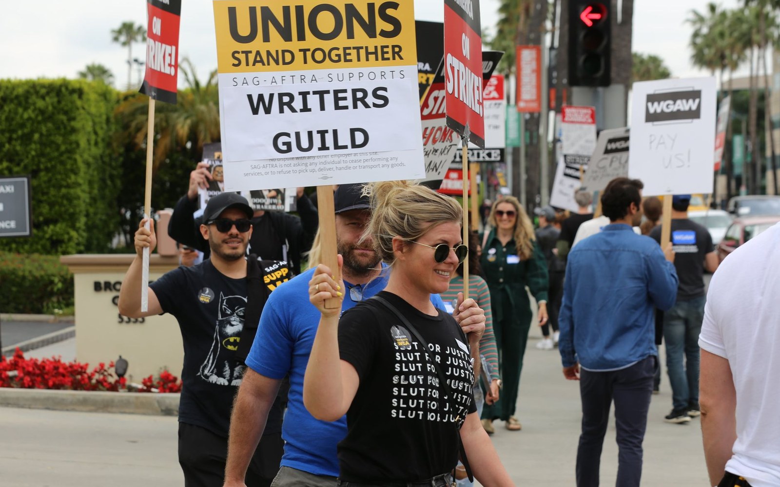 Adult workers on a picket line outside a platform company office, holding printed placards, shot at street level